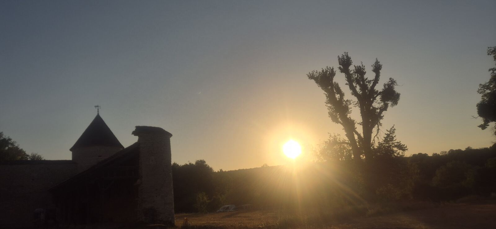 Le soleil se couche sur la colline boisée, à côté de la tour ronde et des communs